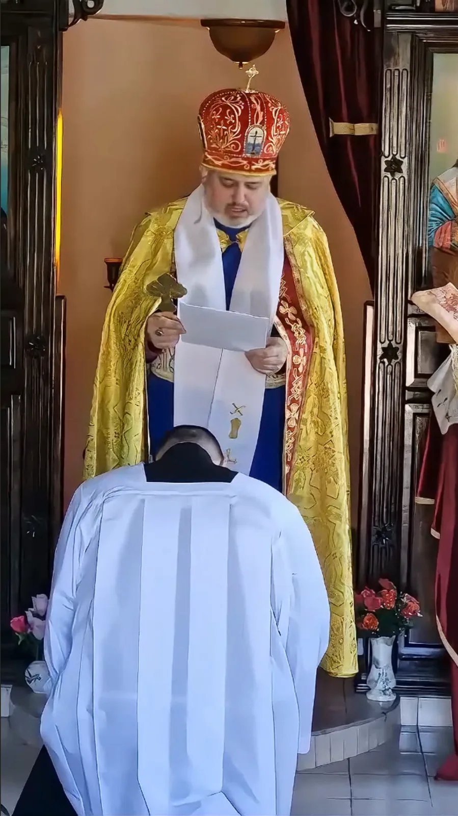 Bishop Ashley Deutschmann kneeling during an Eastern-rite service while a bishop reads prayers